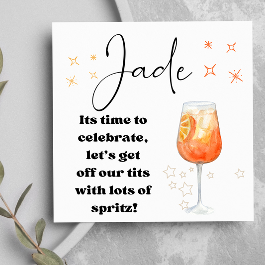 A square white greeting card for a celebration like a birthday. It has a name at the top in a cursive font. Underneath it says “it’s time to celebrate, let’s get off our tits with lots of spritz”. Image of a glass of aperol spritz!